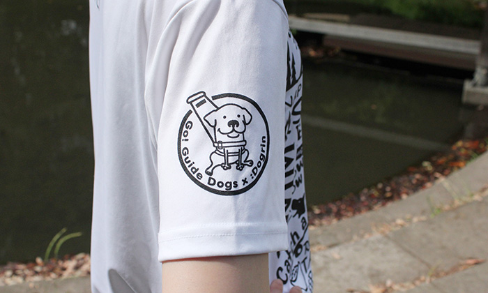 右袖アップ。白のTシャツに黒のプリント。丸の中に盲導犬が描かれている。