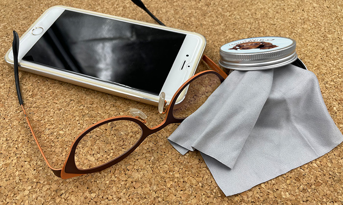 左側にスマホとメガネが置かれている。右側には缶からレンズ拭きが出た状態で置かれている。