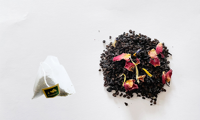 左にティーバック。右に紅茶の茶葉が広げられている。茶葉はローズレッドやマリーゴールド。コーンフラワーといった花びらで彩られている。