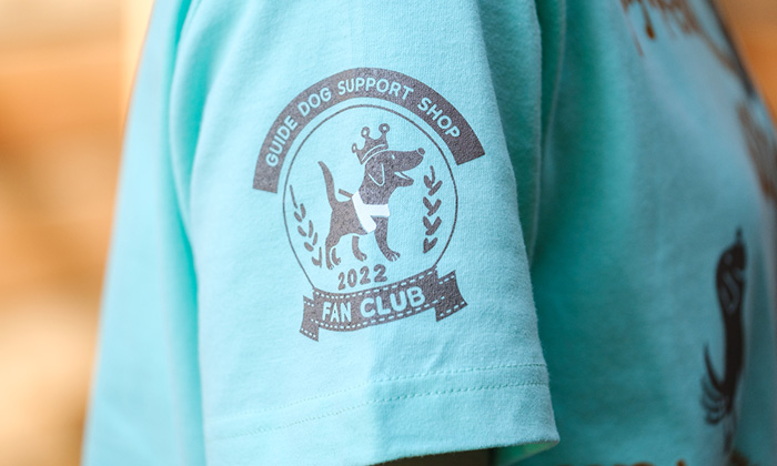 袖のデザインアップ。エンブレムのような形になっている。Guide dog support shopという英文の下に王冠を被った盲導犬のイラスト。一番下に2022 fan clubと書かれている。