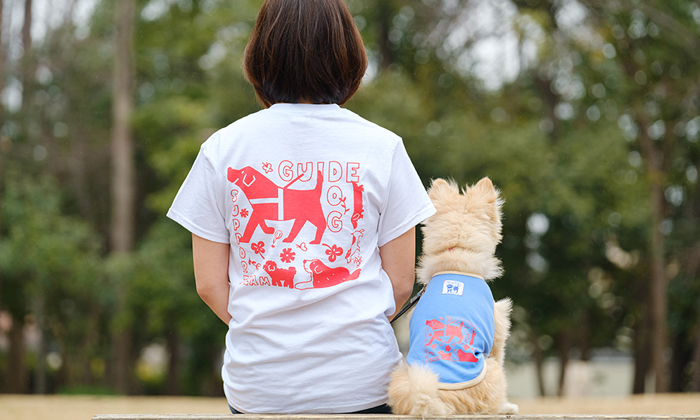 女性モデルが。モデル犬とお揃いのTシャツを着ている。モデル犬と椅子に並んで座っている後ろ姿の写真。
