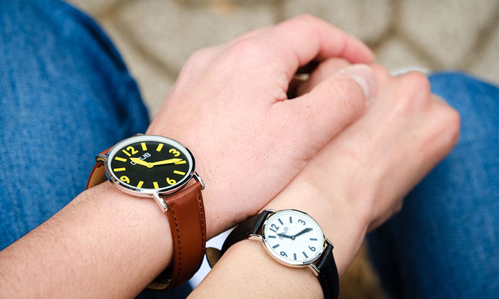 男女で違う時計を身に付けている。男性が女性の手に重ねるようにして握っている。男性は文字盤ブラック。女性は文字盤ホワイトの腕時計を付けている。