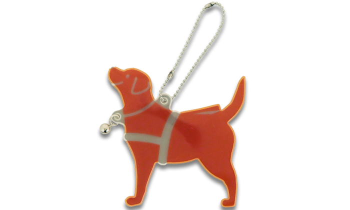 盲導犬の形をしているリフレクター。オレンジをベースに。ニコッとした表情や。ハーネスが白地で描かれている。