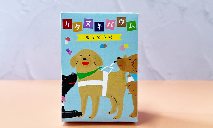 パッケージの写真。長方形のパッケージ。上の部分にはカタヌキバウムもうどう犬と商品名が書かれている。パッケージ正面は。下地が水色にいろんな色の色紙がちりばめられている。