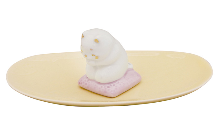 猫の香立ての写真。白い猫が。ピンクの座布団の上にお祈りしながら正座している陶器の香立て。香皿の色は黄色。