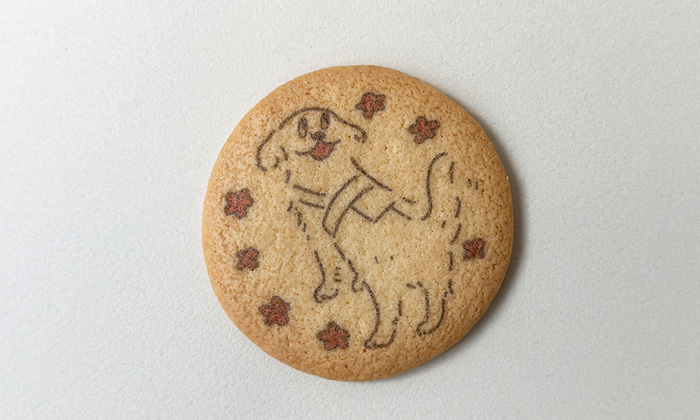 プリントクッキーの写真。ゴールデンレトリバーの盲導犬が笑顔で振り向いているイラストに、周りには赤い花が散りばめられている