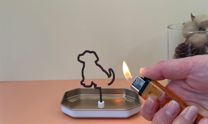 犬のシルエットのお線香にライターで火を付けている写真。