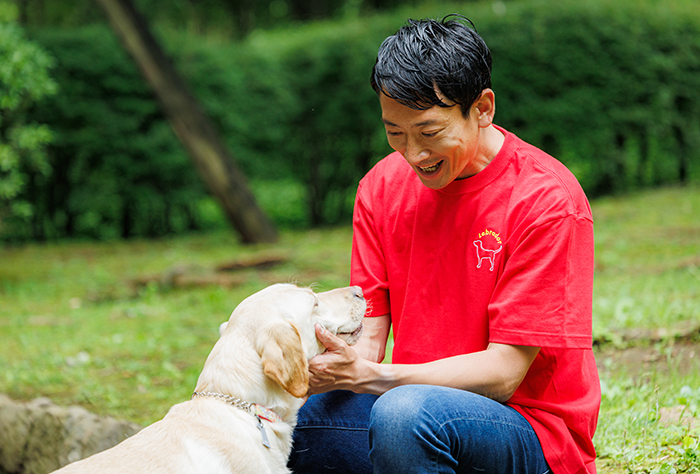 男性がラブラドール刺しゅうのレッドのTシャツを着て、ラブラドールを撫でている写真