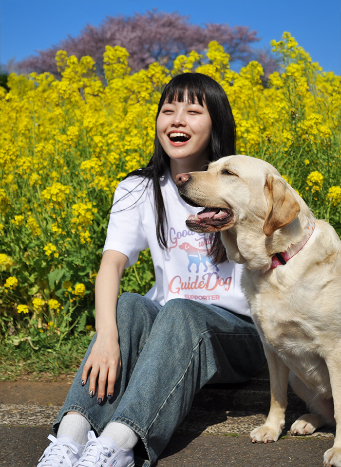 女性モデルがホワイトTシャツにサンセットオレンジ色の盲導犬サポーターデザインのシルエットを着た正面写真
