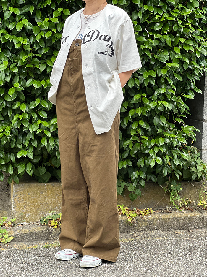 茶色のオーバーオールに黒のロゴのベースボールTシャツを羽織っている写真