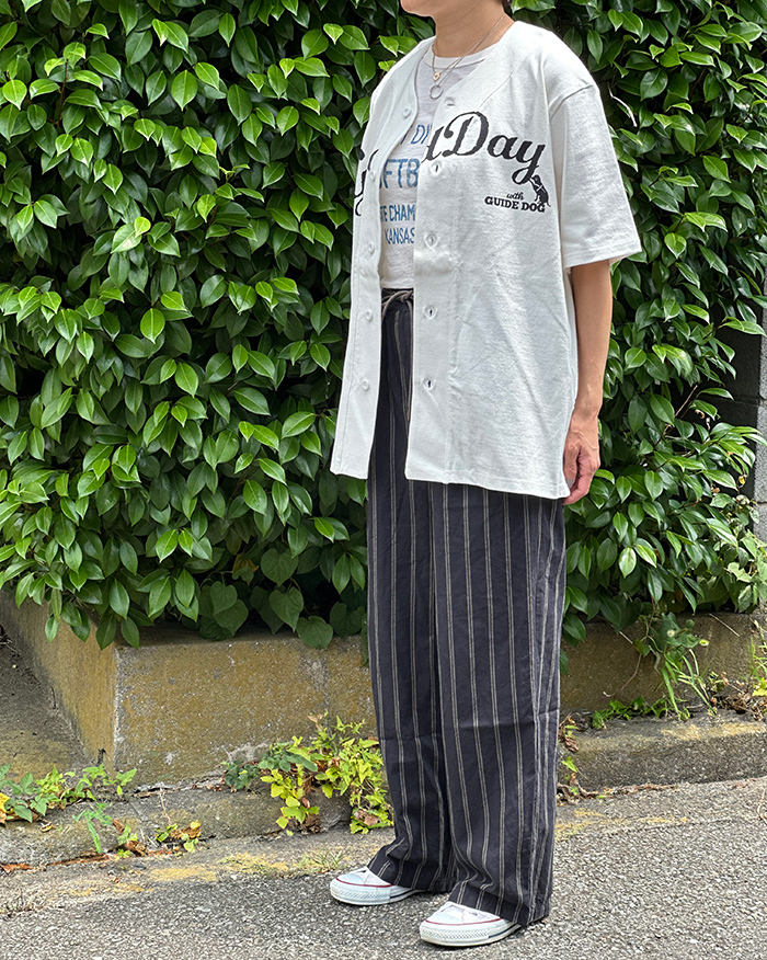 黒とベージュのストライプパンツの上に白いTシャツの上からに黒のロゴのベースボールTシャツを羽織っている写真