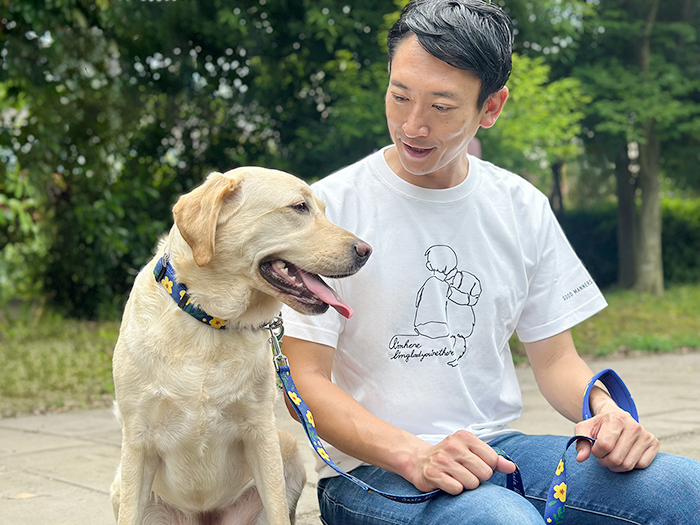 男性がホワイトのTシャツを着て、ラブラドールと隣同士で座っている写真