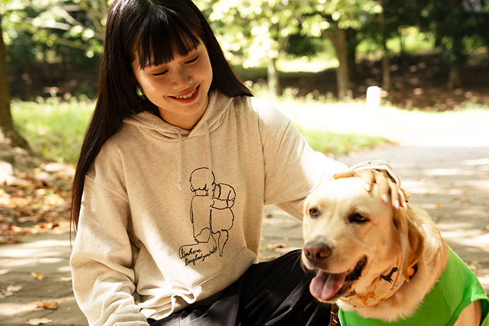 女性がプリントのオートミールのフーディーを着て、ラブラドールと隣同士で座っている写真