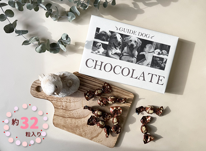 盲導犬とパピーの7枚の写真が配置された包装紙に包まれた箱と中身の包み紙に包まれたチョコレート