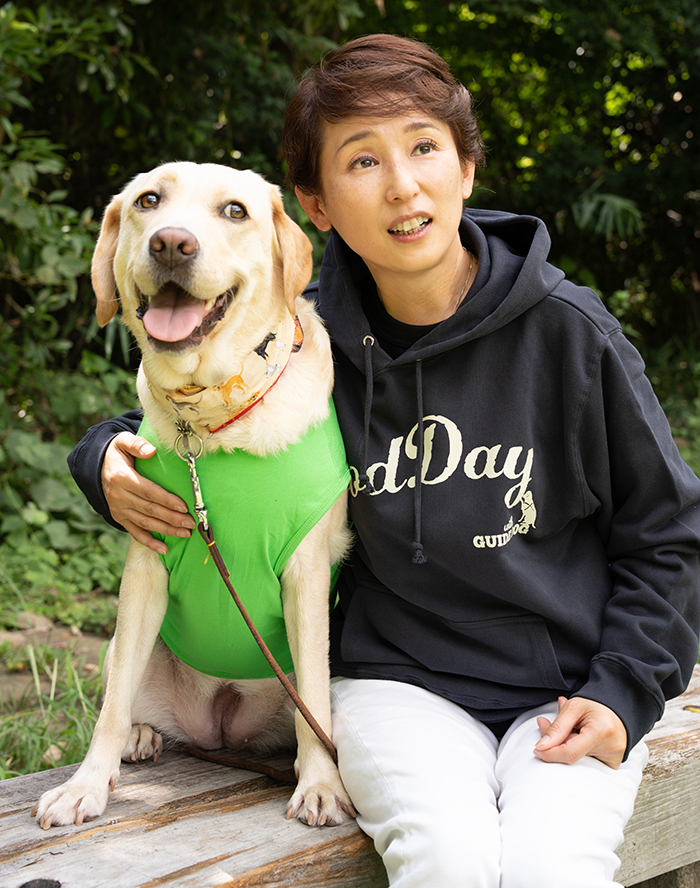 女性がホワイトジーンズの上にネイビーのパーカーを着て、笑顔のラブラドールに肩を回して座っている写真