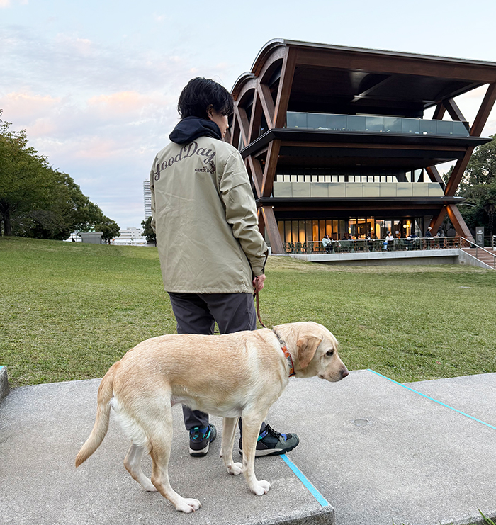 女性がネイビーのパーカーの上からジャケットを着てスウェットにスニーカーを履いてラブラドールと散歩している写真