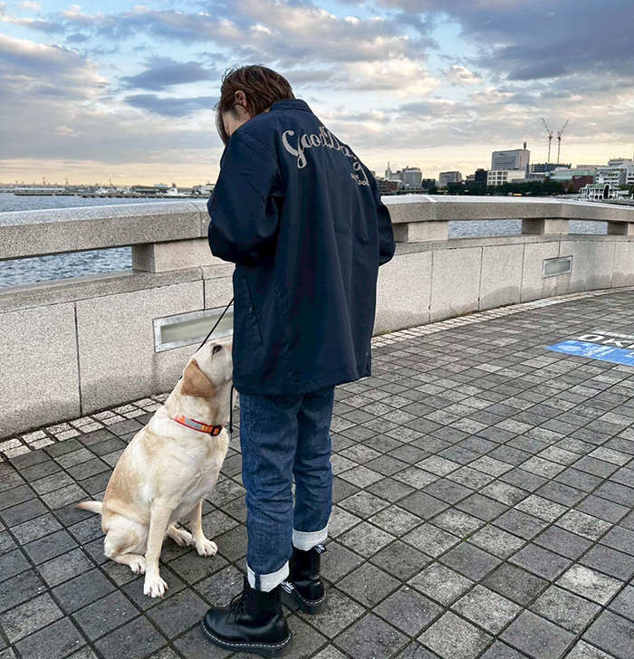 女性がネイビーのジャケットを着用し、後ろを向いて下にいるラブラドール見つめあっている写真