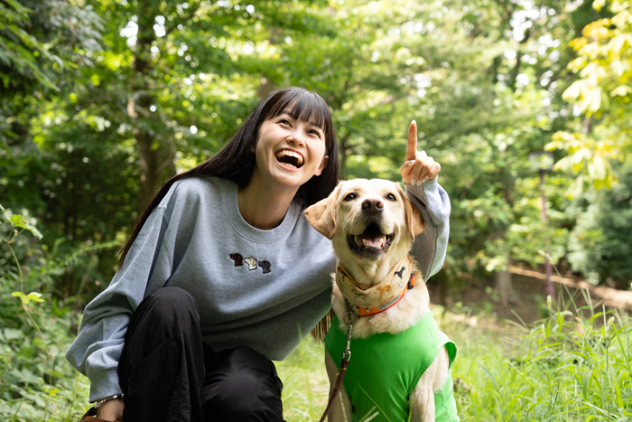 女性とラブラドールがしゃがみ揃って笑顔で空を見上げている写真