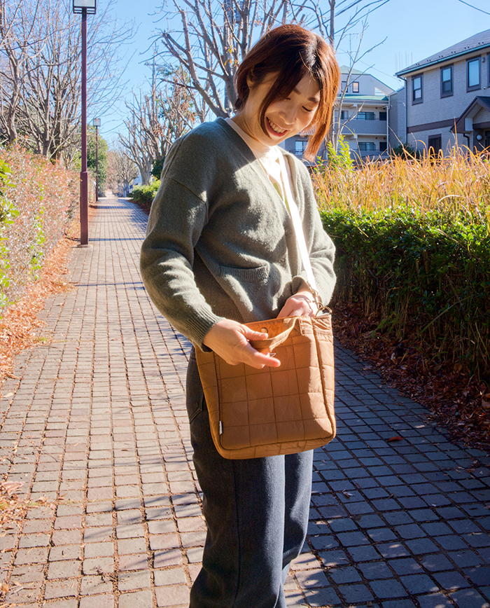 女性がブラウンのバッグを斜め掛けしたまま、バッグの中を見ている写真