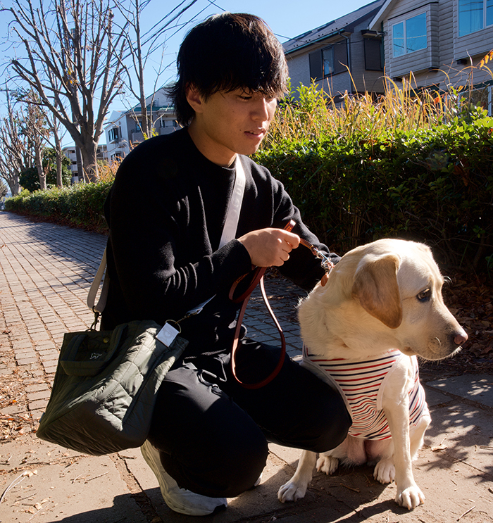 男性がラブラドールの横にしゃがみカーキのバッグを斜め掛けしている写真