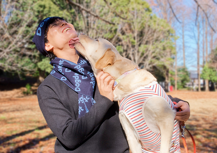 男性がネイビーのニットキャップとマフラーをしラブラドールと楽しそうにしている写真