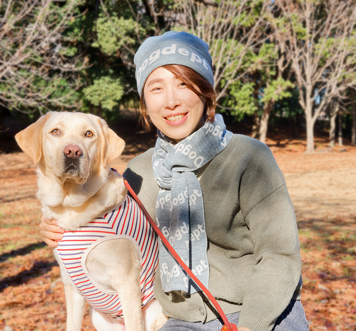 女性がミックスグレーのニットキャップとマフラーを着けてラブラドールと寄り添っている写真