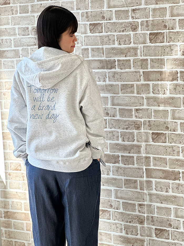 女性がネイビーのゆったり目のパンツにアッシュのパーカーを着てポケットに手を入れて背を向けてブルーのプリントが見えている写真