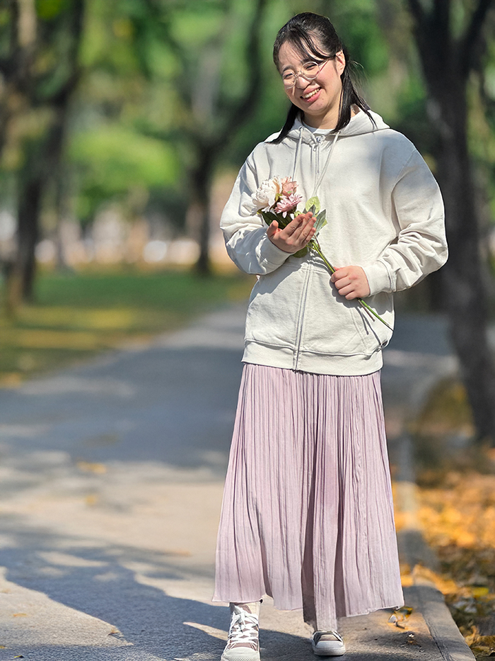 女性がピンクのふわっとしたスカートにグレージュのパーカーを着て花を持っている写真