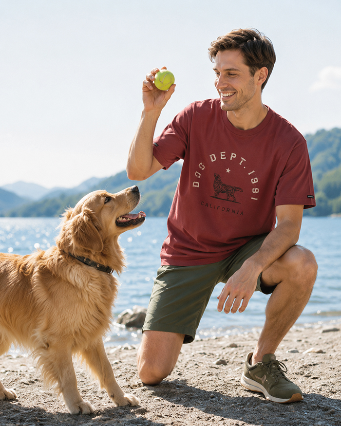 男性がワイン色のTシャツを着用し、ゴールデンレトリーバーと遊んでいる写真