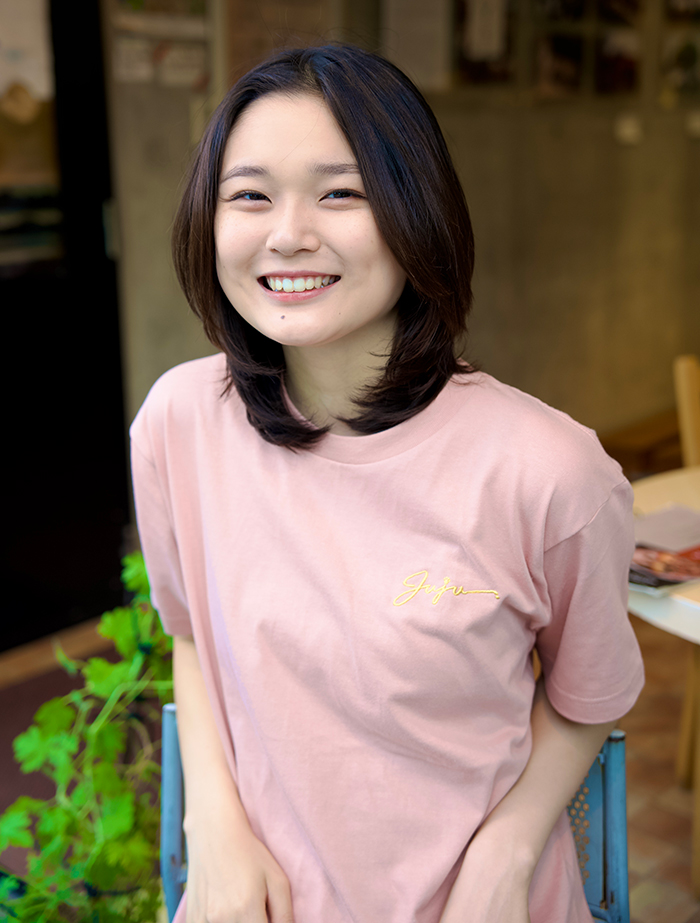 Juju選手がダスティピンクのTシャツを着て椅子に座り正面を向いている写真