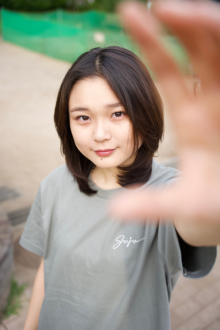 Juju選手がモスグレーのTシャツを着て正面を向いてカメラに手を伸ばしている写真