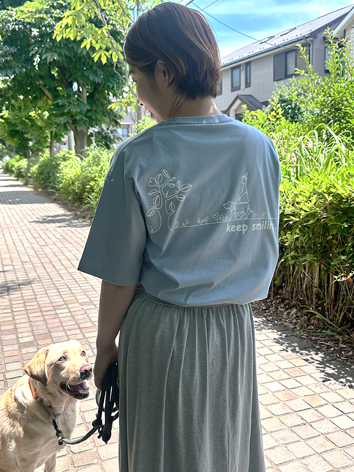 女性がアシットブルーのTシャツの下にグレーのスカートを着用しラブラドールと散歩をしている写真。