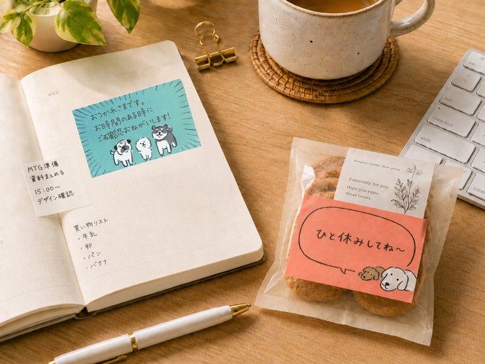 デスクの上の自分の手帳に忘れないようにふせんに必要事項を書き貼っているのと、小分けのクッキーののパッケージにメッセージが書かれている写真